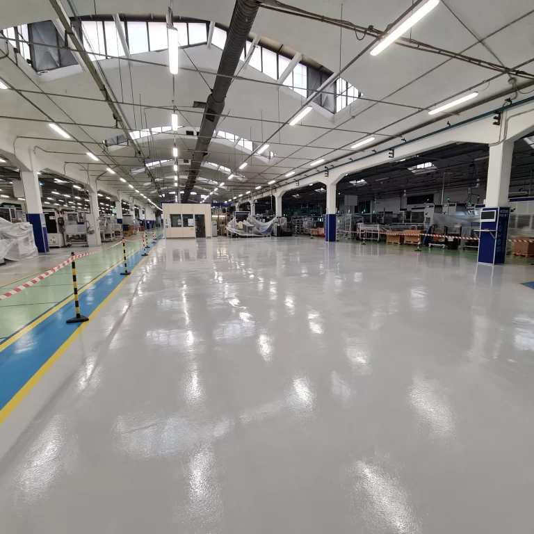 Pavimento in resina lucida in un ambiente industriale ampio, con macchinari e corsie delimitate per la sicurezza.