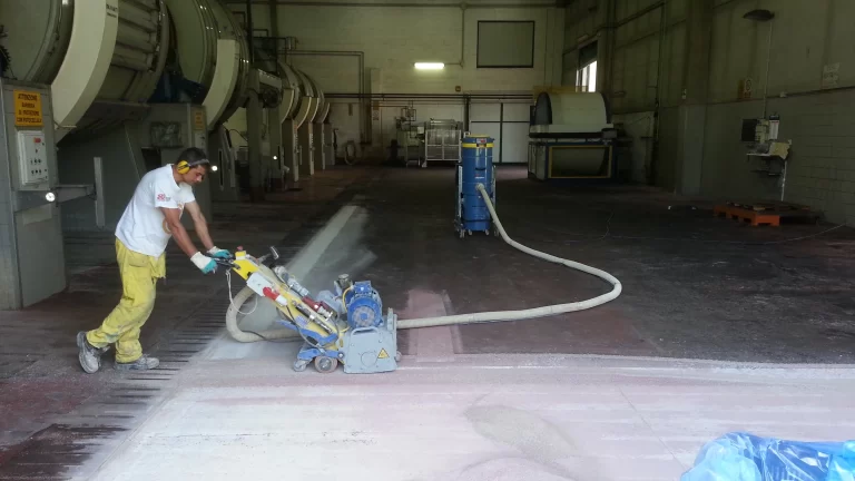 Tecnico utilizza una macchina per la preparazione del pavimento in un ambiente industriale, rimuovendo la superficie per l'applicazione della resina.