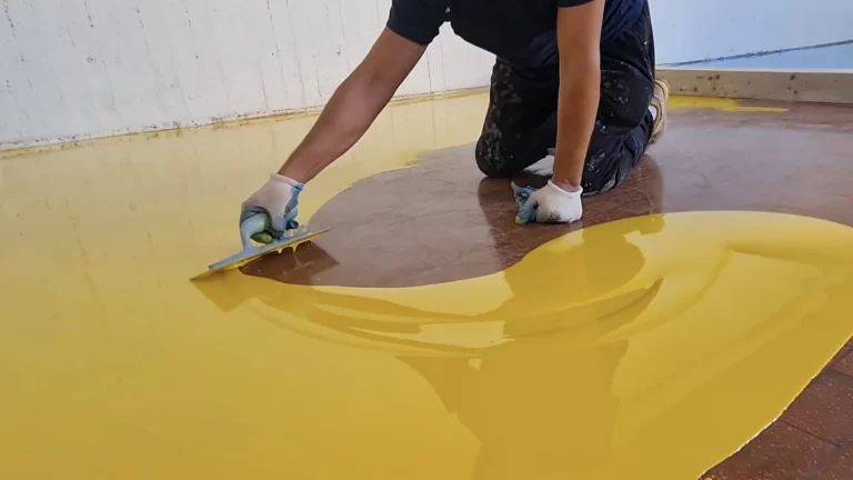 Esperto che applica resina epossidica autolivellante gialla su un pavimento utilizzando una spatola dentata.